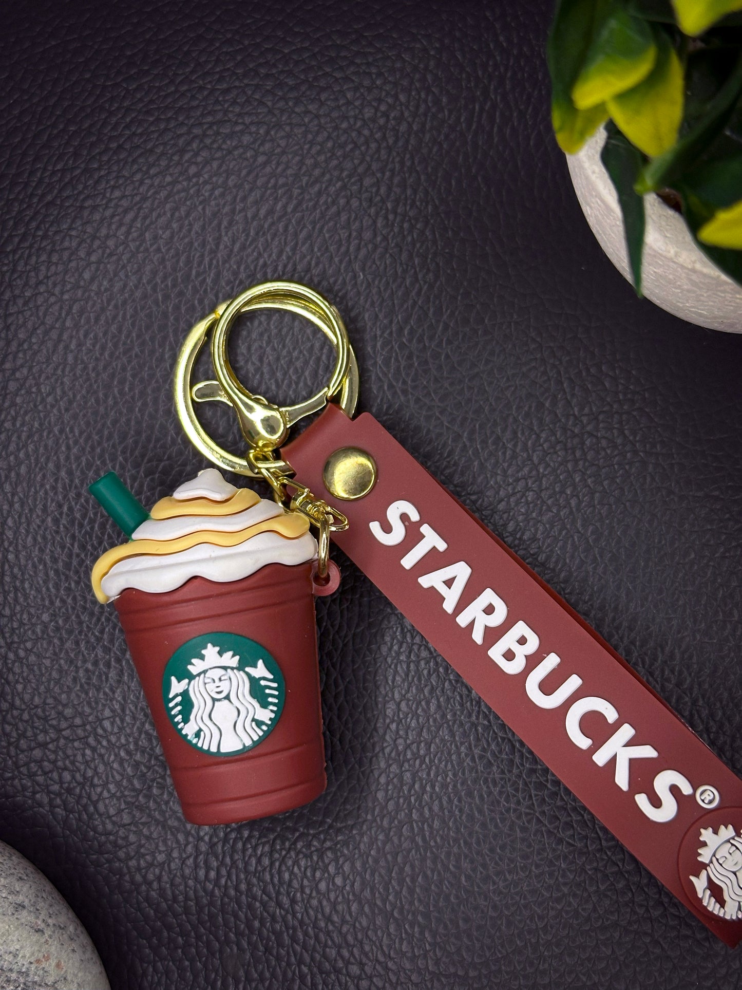 A green Starbucks frappuccino-shaped keychain with a whipped cream top and caramel drizzle, attached to a green rubber strap with the Starbucks logo, finished with a golden keyring.