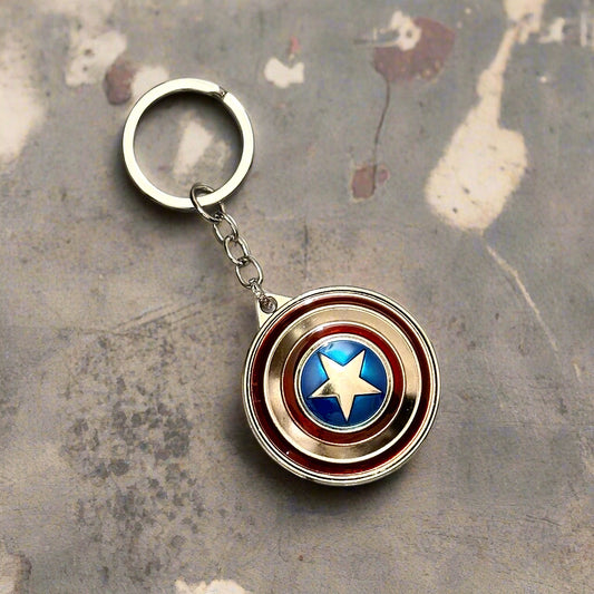 A Captain America shield-themed keychain with a metallic red, silver, and blue spinner design placed on wooden slices with a plant in the background.