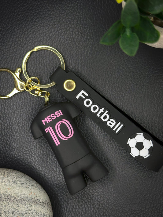 A Messi #10 black football jersey-shaped keychain with a matching black strap labeled “Football” and a white soccer ball icon.
