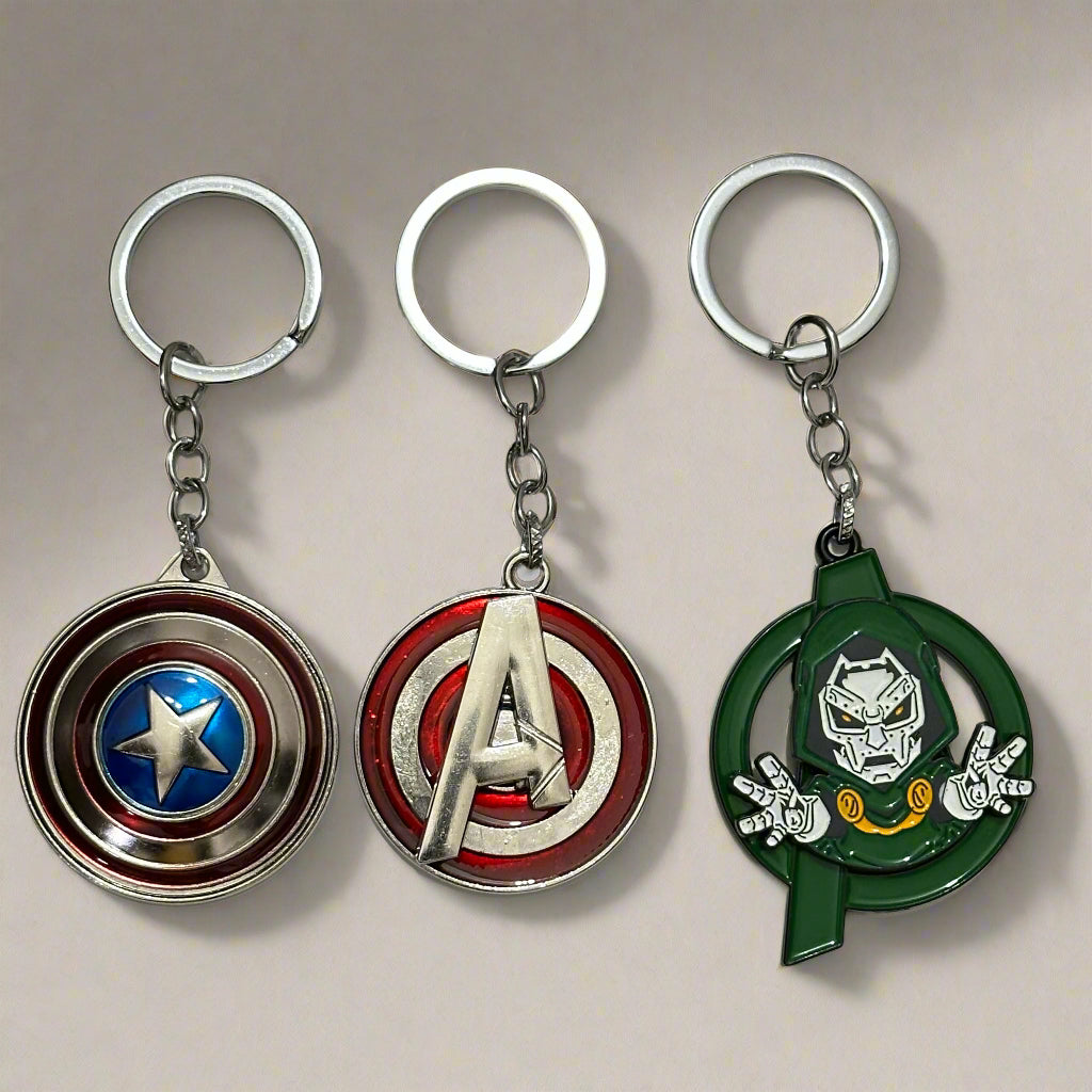 A set of three Marvel spinner keychains featuring Captain America’s shield, a red Avengers “A” logo, and Doctor Doom in a green circular spinner frame—styled on a white marble hexagon-tiled surface.