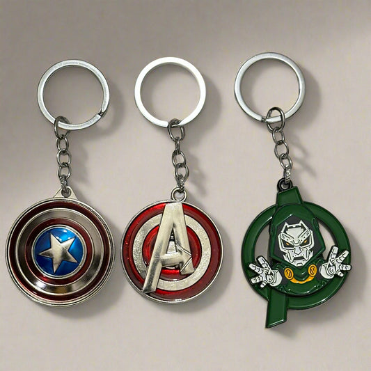 A set of three Marvel spinner keychains featuring Captain America’s shield, a red Avengers “A” logo, and Doctor Doom in a green circular spinner frame—styled on a white marble hexagon-tiled surface.
